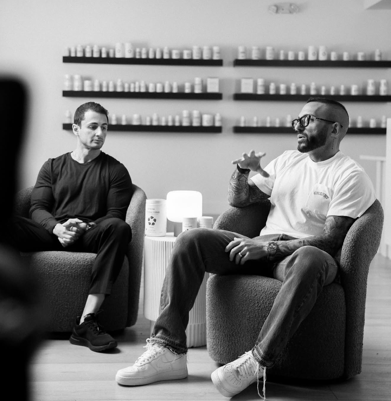 Dominic Kuza in conversation with Dom Iacovone, seated in front of shelves of supplement products
